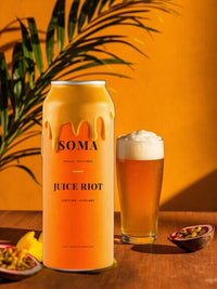 SOMA IPA can with a hazy golden pour among tropical leaves